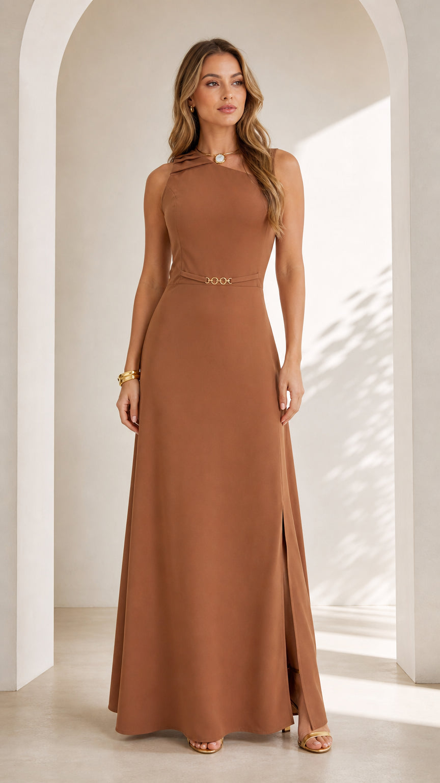 Front full view of woman wearing caramel brown sleeveless asymmetrical maxi dress with chain waist detail