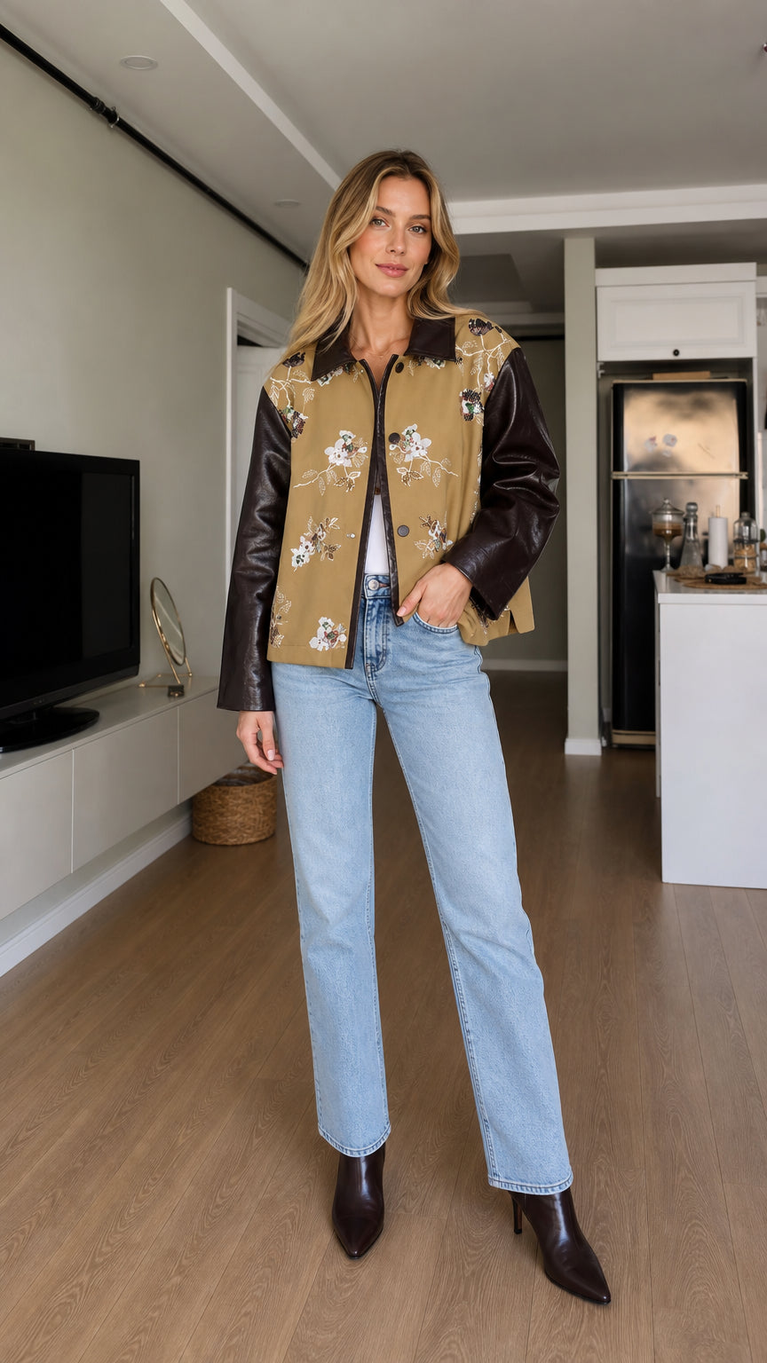 Full-body front view of model wearing camel floral embroidered jacket with dark brown faux leather sleeves and light blue jeans