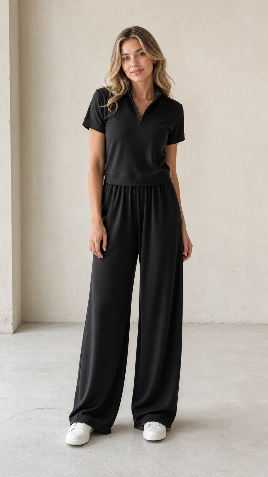 Front full-length view of woman wearing black half-zip short-sleeve top and wide-leg matching pants set