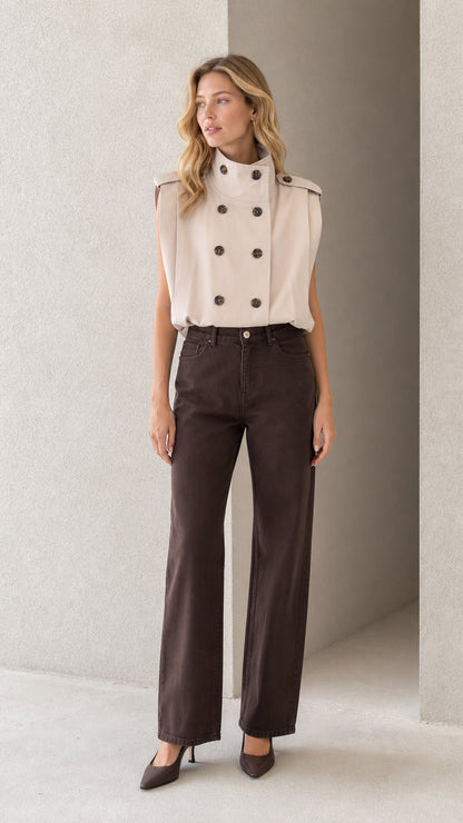 Front view of model wearing beige sleeveless high neck double-breasted trench top with dark trousers