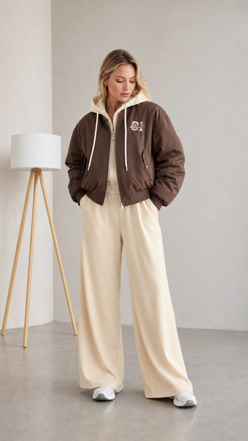 Front full view of woman wearing brown layered hooded bomber jacket with cream wide-leg pants