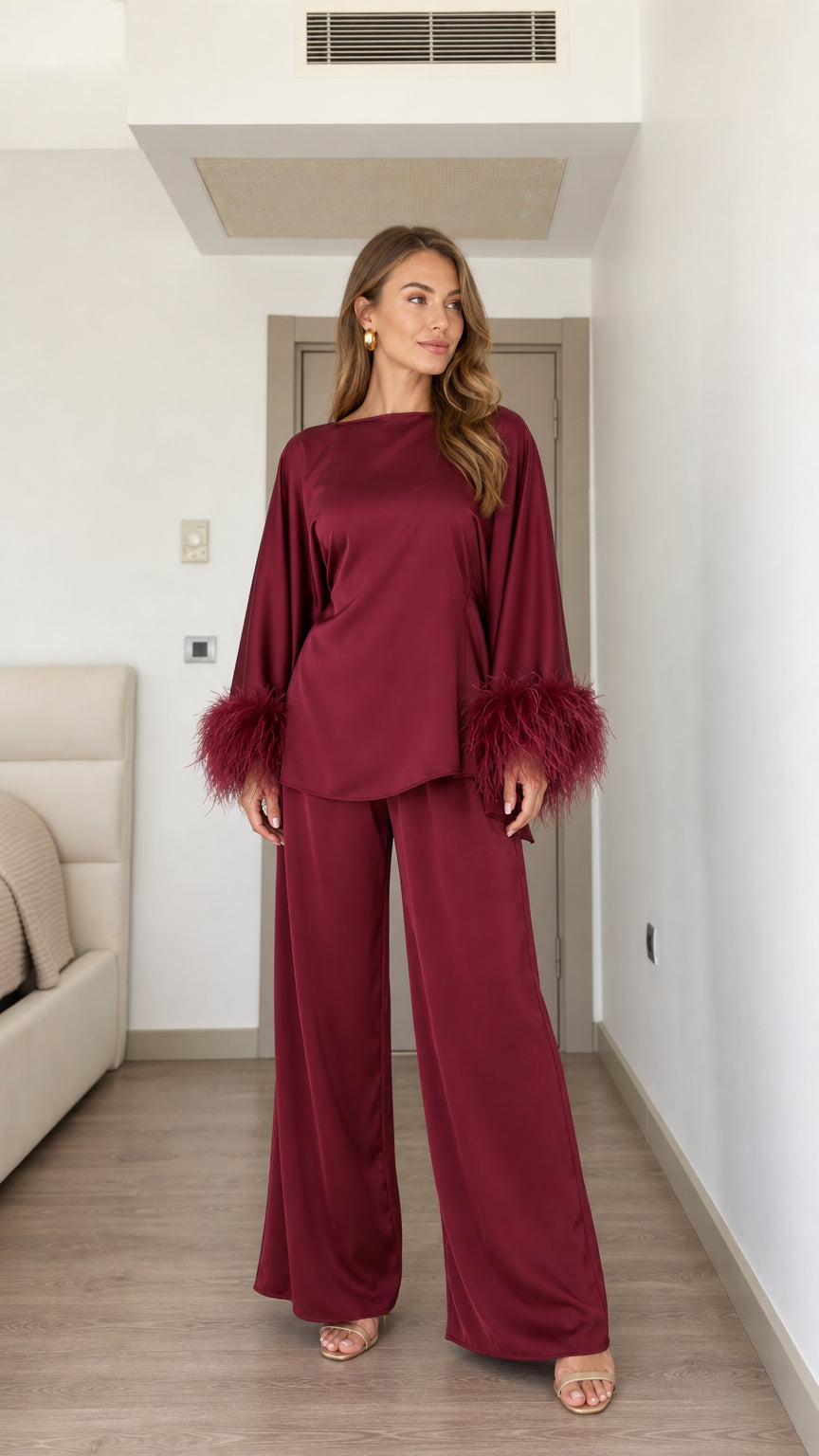 Front view of woman wearing burgundy satin matching set with feather cuffs