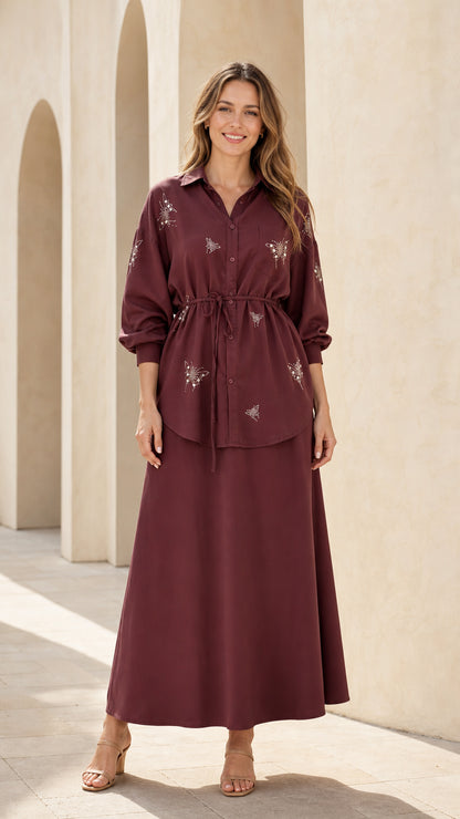 Front view of woman wearing burgundy embellished button-down tunic top and maxi skirt set