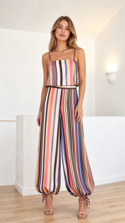 Front full-length view of model wearing vibrant multicolor striped satin cami jumpsuit with tie ankle cuffs