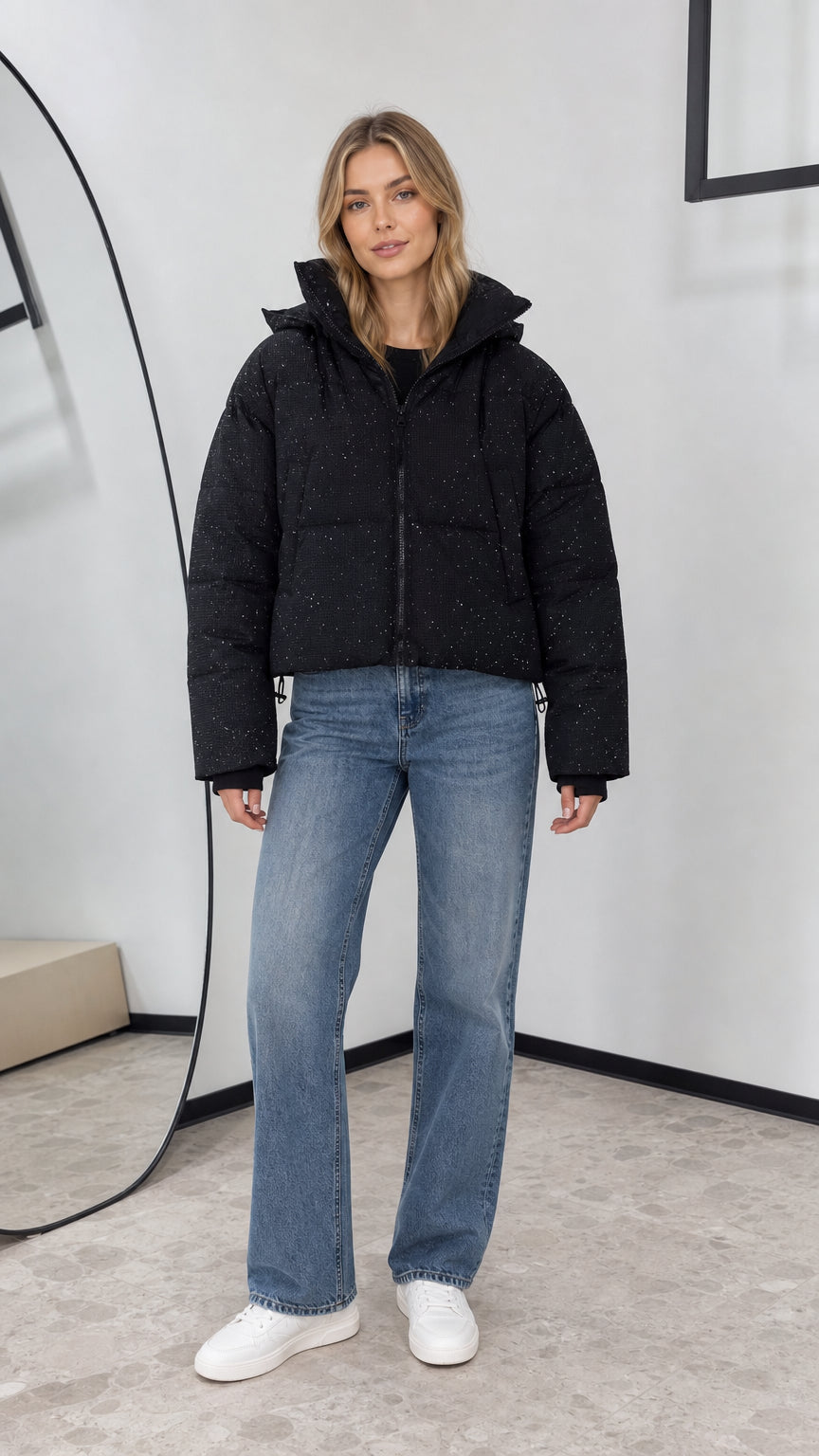 Front view of woman wearing black shimmer cropped hooded puffer jacket with wide-leg jeans