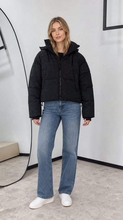 Front view of woman wearing black shimmer cropped hooded puffer jacket with wide-leg jeans