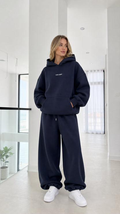 Front full-length view of model wearing the navy oversized hoodie and sweatpants set with white sneakers