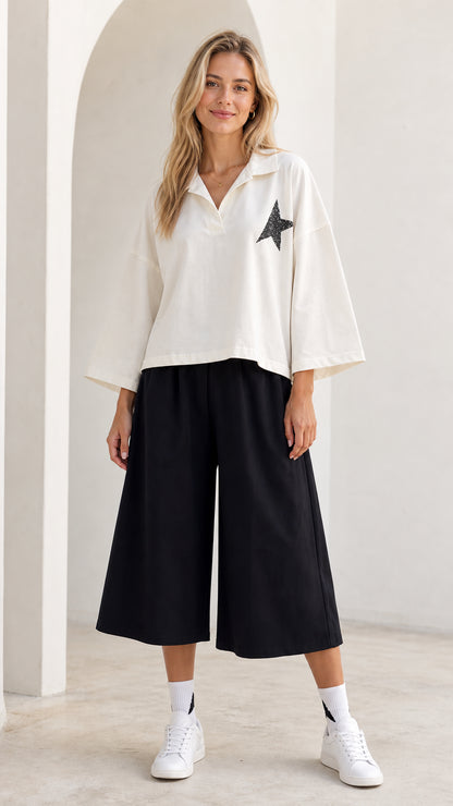 Front full-length view of model wearing white star polo top and black culotte pants