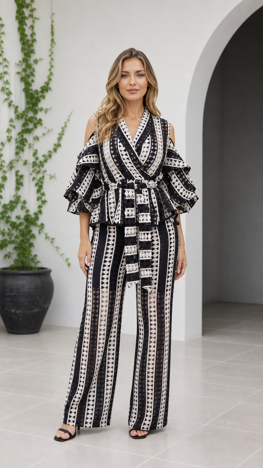 Front full-length view of woman wearing black and white geometric cold shoulder wide-leg jumpsuit with belt
