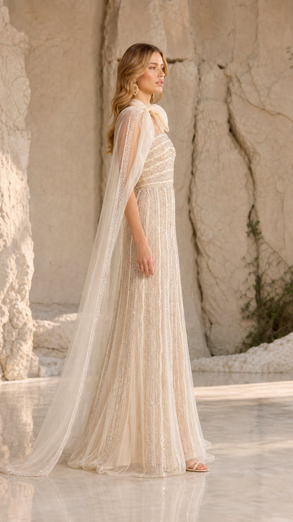 Side profile of champagne beaded formal dress showing cape drape and bodice details