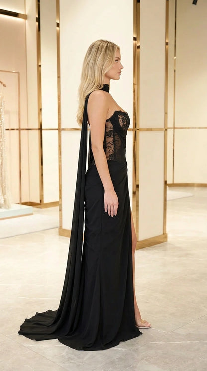 Side profile of model wearing black lace corset evening dress showing floor-length flowing shoulder sash