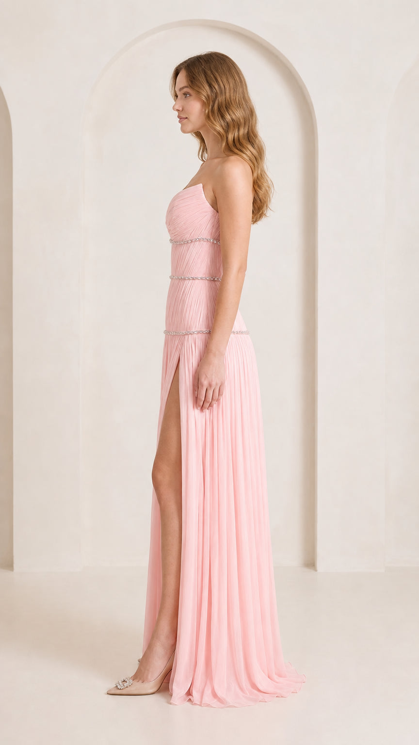 Side profile of woman in strapless blush pink pleated maxi gown showing thigh-high leg slit