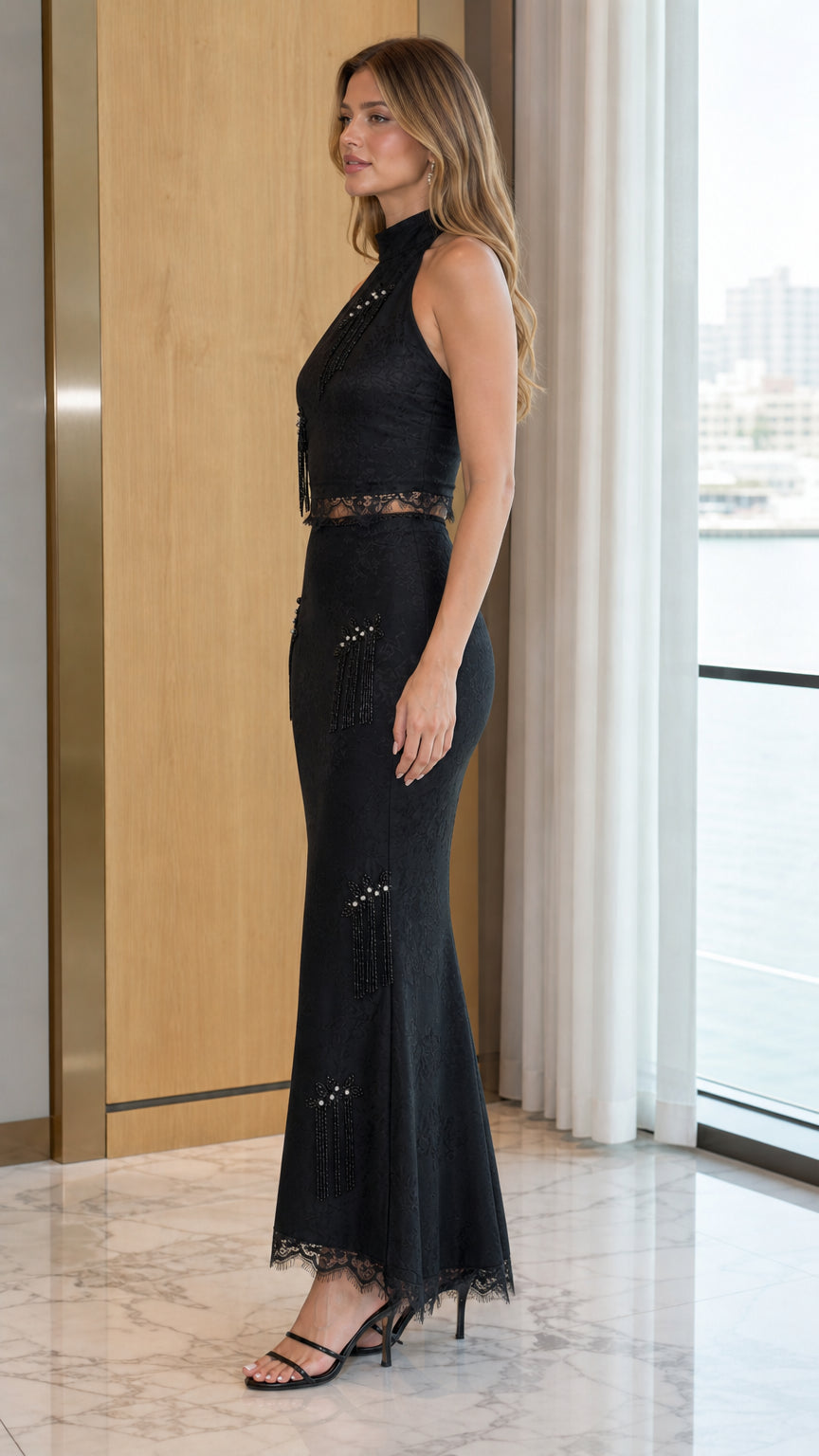 Side profile view of model wearing black halter neck evening gown with beaded fringe