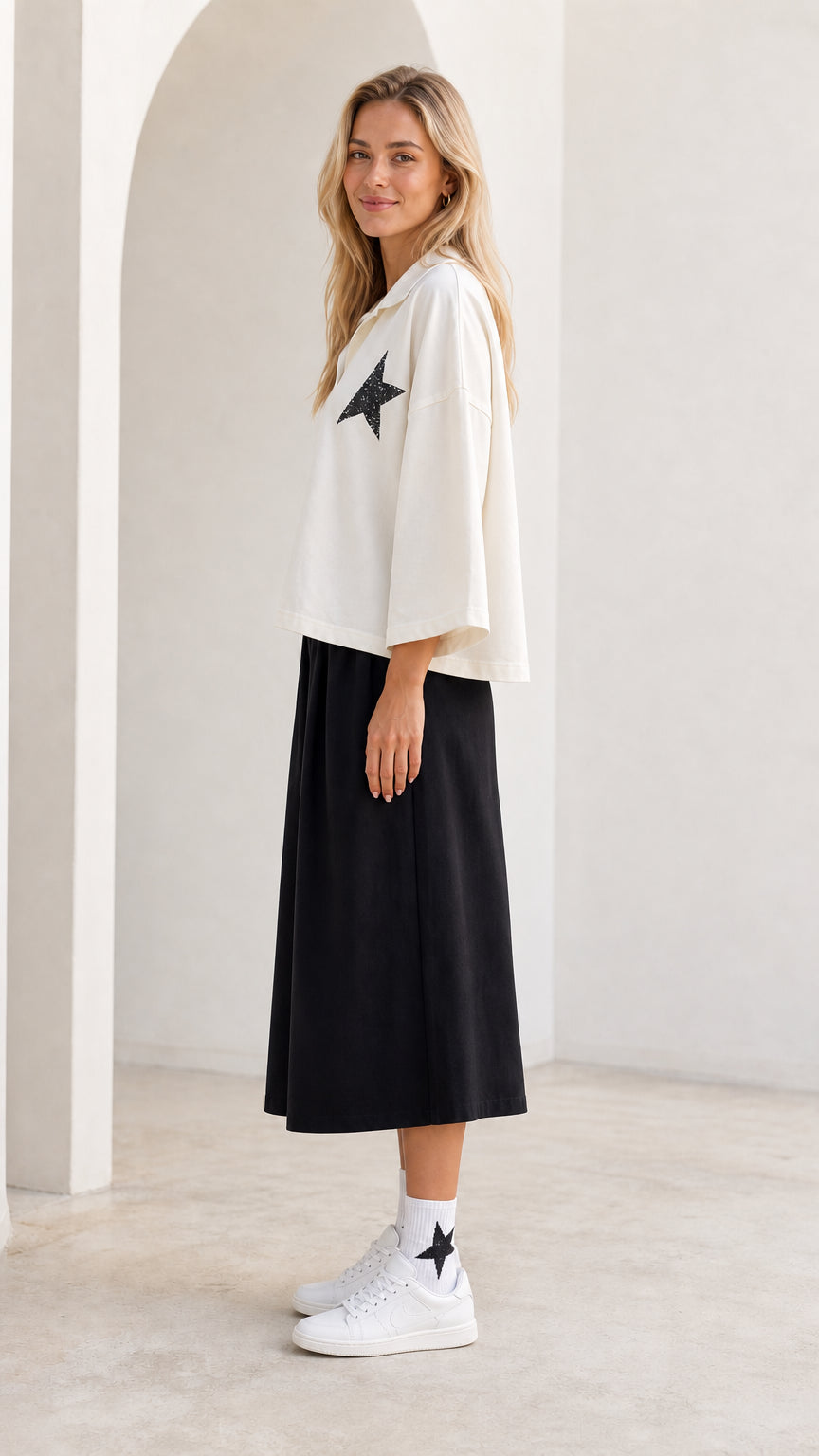 Side profile view of model wearing white star graphic collared top and black cropped pants