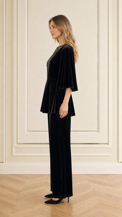 Side profile view of woman modeling black velvet peplum top and wide-leg trousers