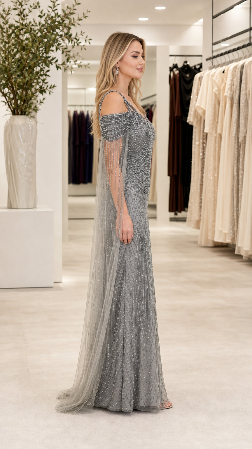 Side profile view of silver beaded formal maxi gown showing cape sleeve drape