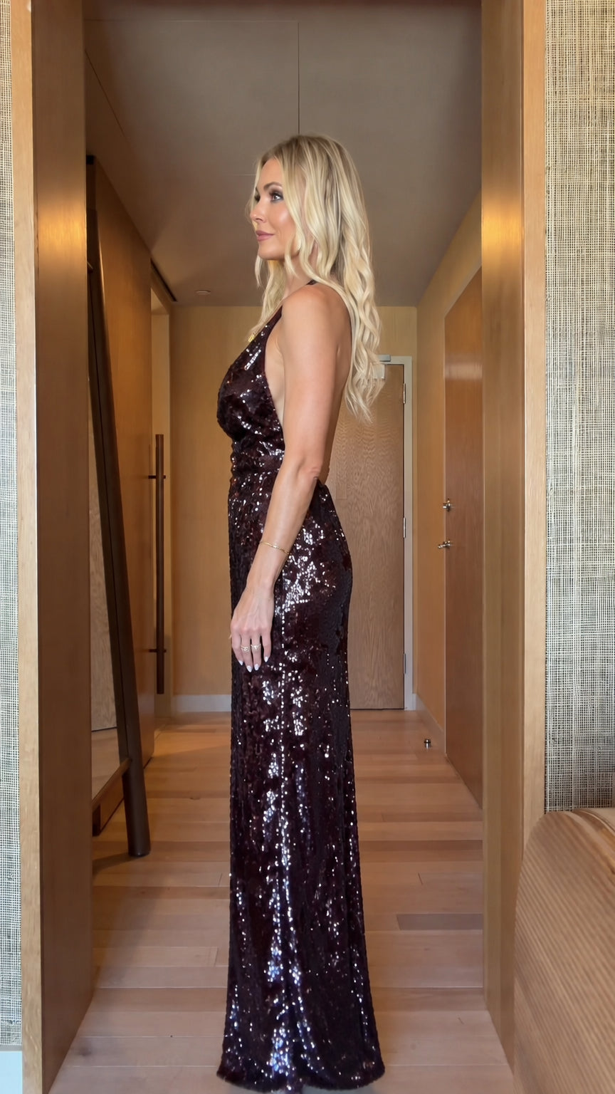 Side profile view of burgundy sequin halter maxi gown showing fitted silhouette