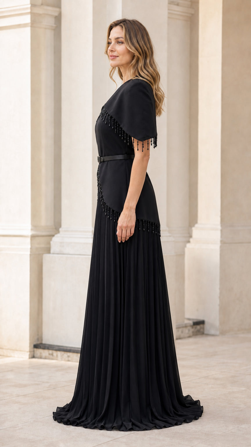 Side profile view of woman wearing black capelet maxi dress with pleated skirt