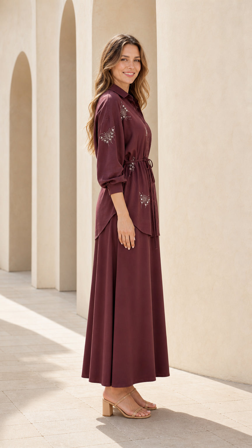 Side profile view of woman modeling burgundy long-sleeve maxi skirt two-piece set