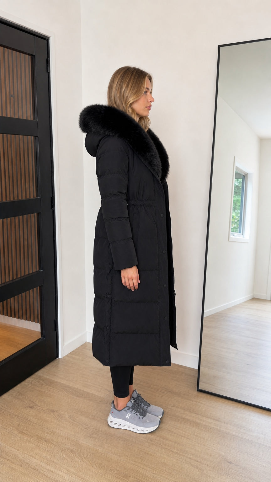 Side profile view of black full length quilted winter coat with hood