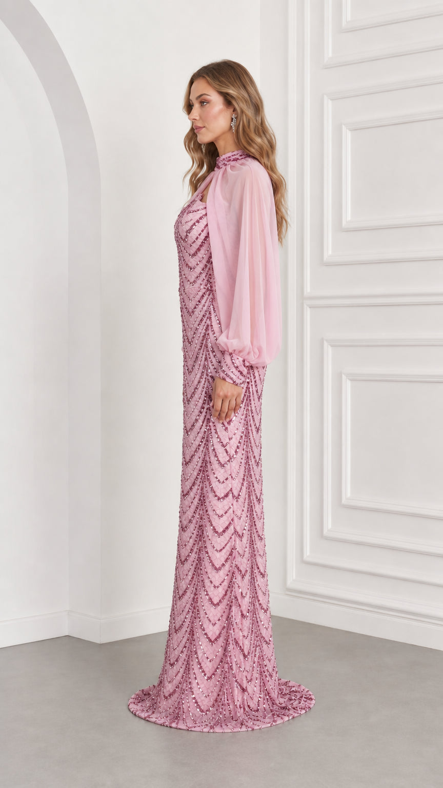 Side profile view of woman wearing pink sequin floor-length formal gown with flowing cape