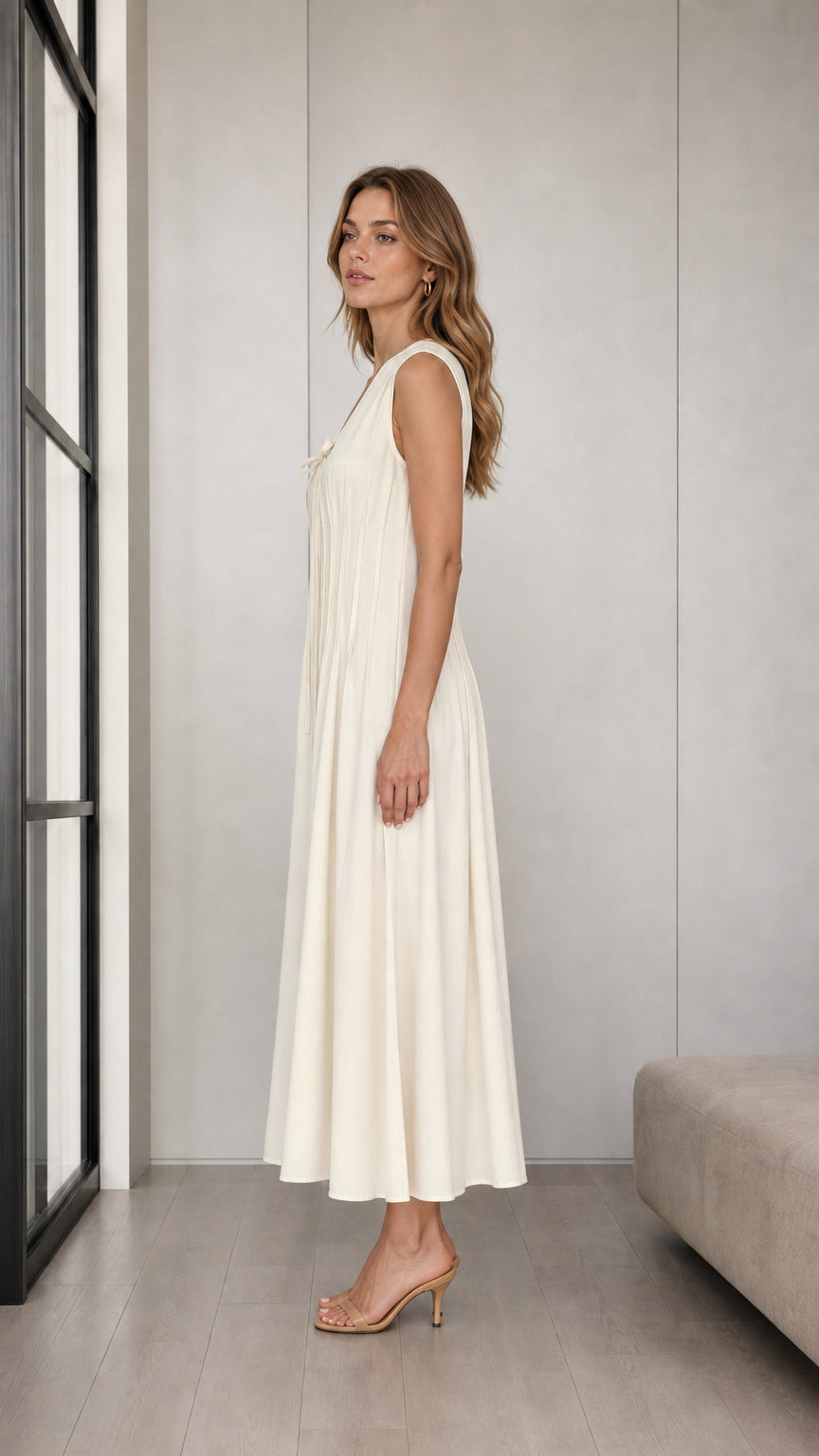 Side profile view of woman modeling Cream sleeveless pleated A-line midi dress