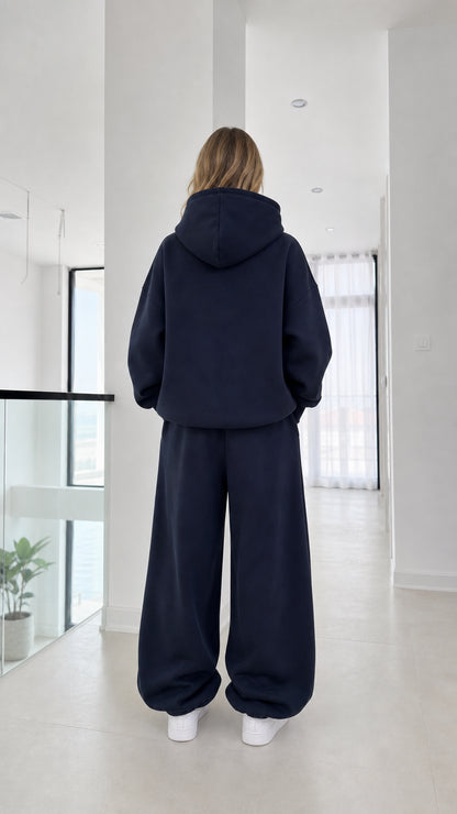 Back full-length view of model in the navy fleece hoodie and sweatpants