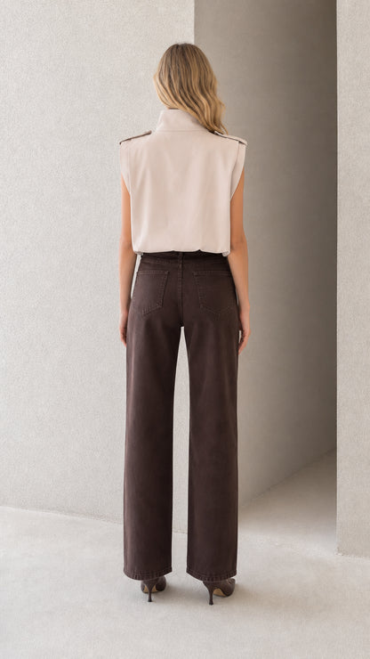 Back view of model wearing beige sleeveless high neck top tucked into brown pants