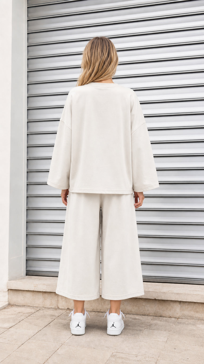 Back view of model wearing relaxed fit cream sweatshirt and matching cropped pants
