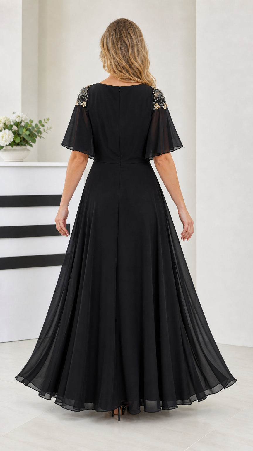 Back view of black flutter sleeve evening gown showing zipper and pleated skirt