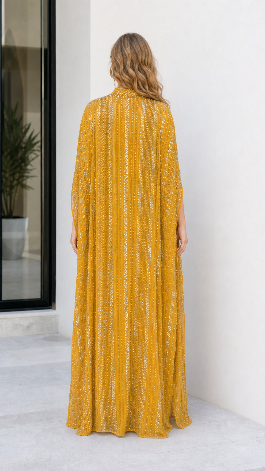Back view of model wearing flowing mustard yellow sequin maxi gown