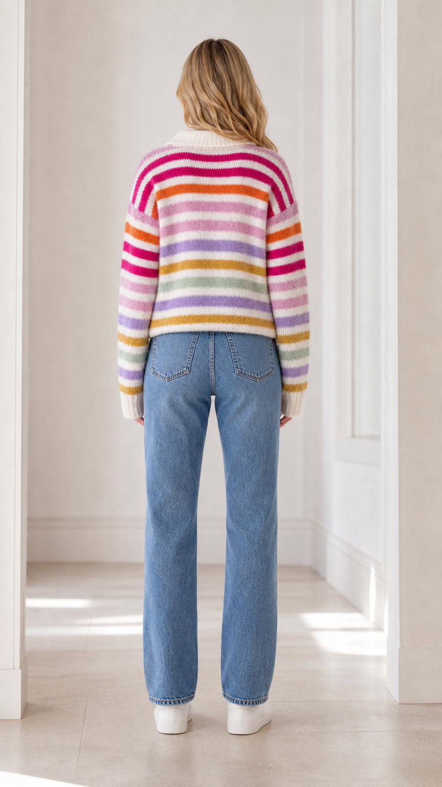 Back full view of woman wearing cream multicolor striped knit sweater and straight-leg denim