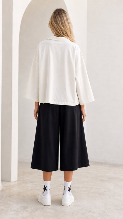 Back view of model wearing white relaxed fit open collar shirt and cropped wide leg pants