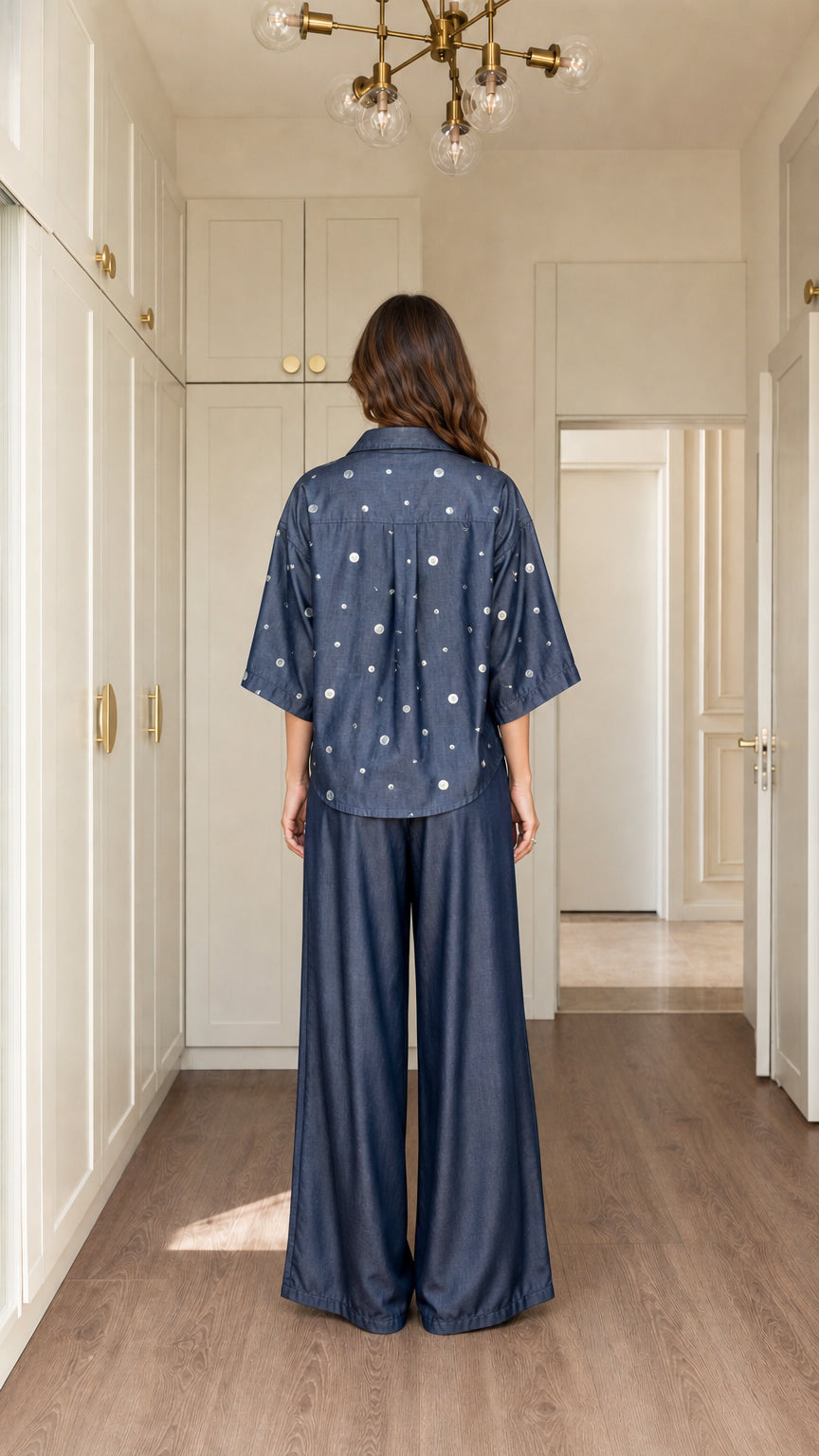 Back view of model wearing Denim Blue polka dot button-down shirt and wide-leg pants
