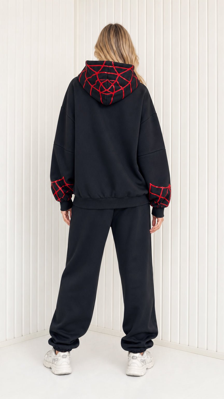 Back view of model showing graphic web details on hoodie of black sweatsuit set
