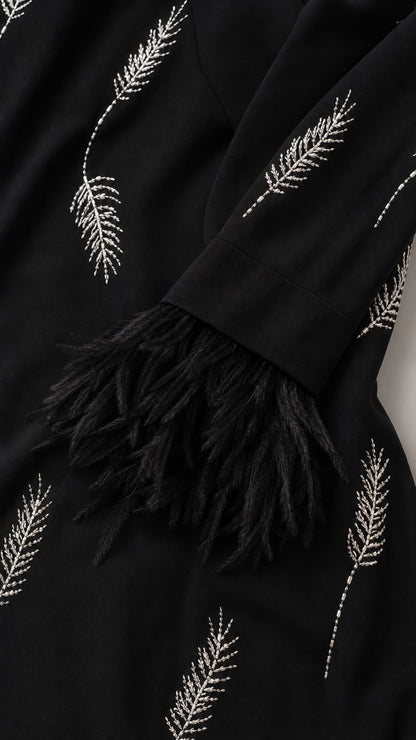 Close up detail of sleeve featuring white leaf embroidery and black feather trim