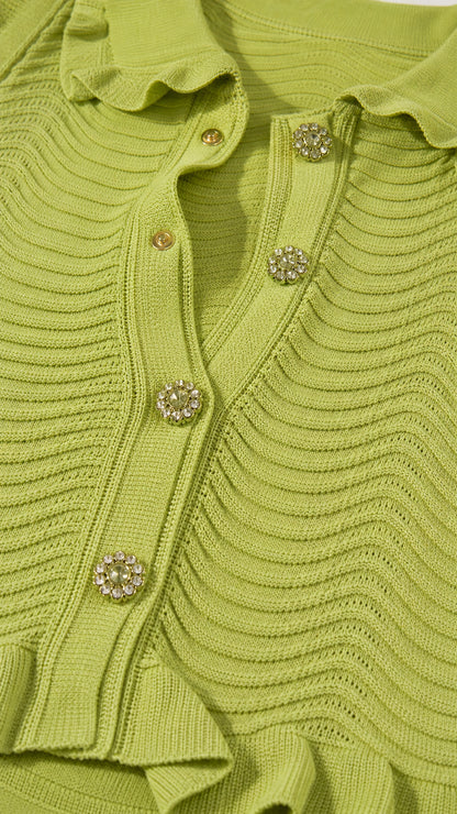 Close-up detail of lime green textured wave knit fabric with ruffle collar and rhinestone buttons