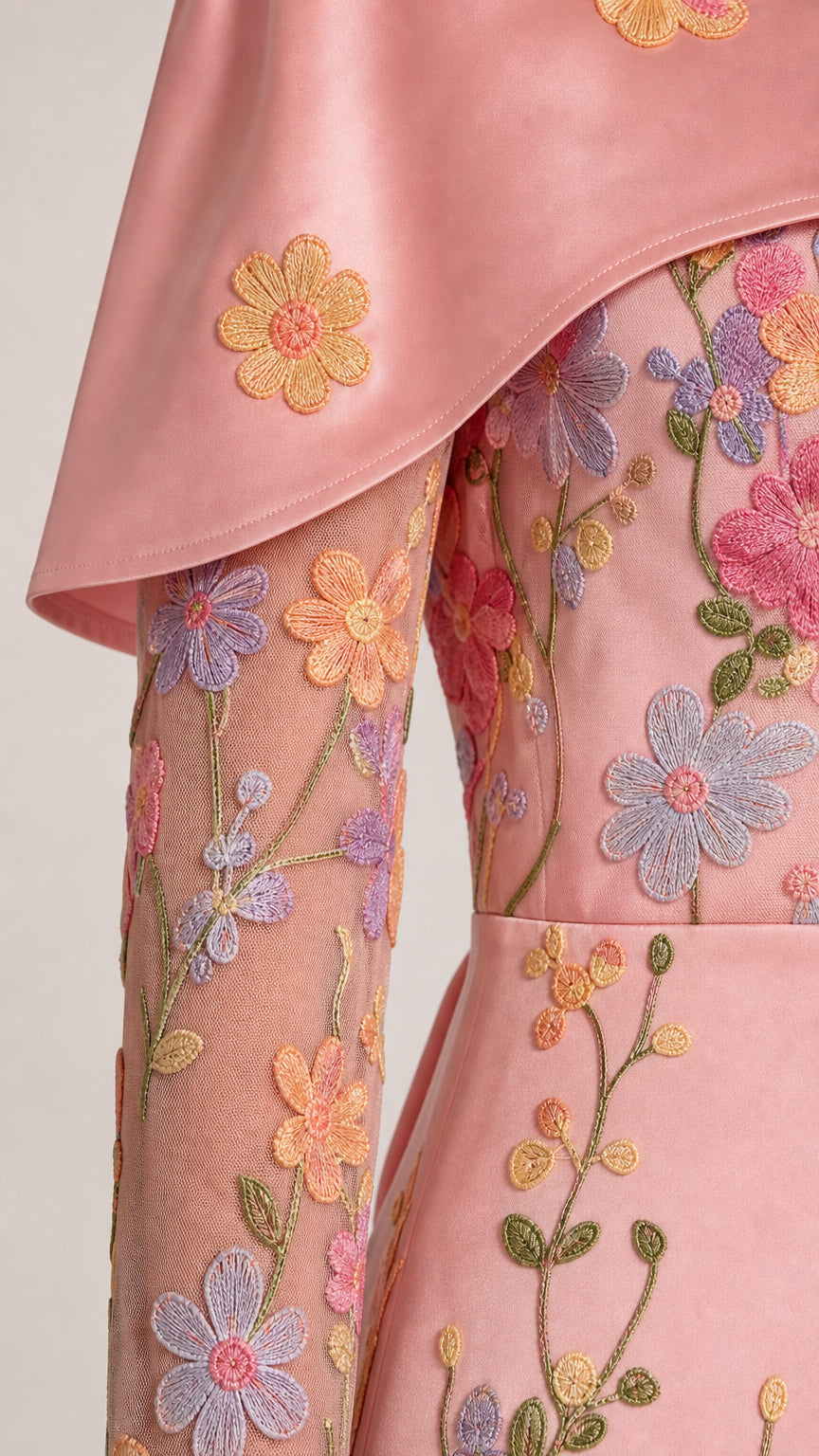 Close-up detail of smooth capelet fabric and colorful 3D floral embroidery on sheer mesh sleeve