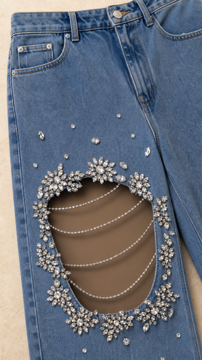Close-up detail of denim cutout with rhinestone trim and horizontal draped chain accents