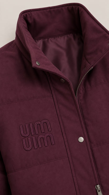 Close-up detail of burgundy stand-collar puffer vest with snap buttons, zipper, and subtle chest embroidery
