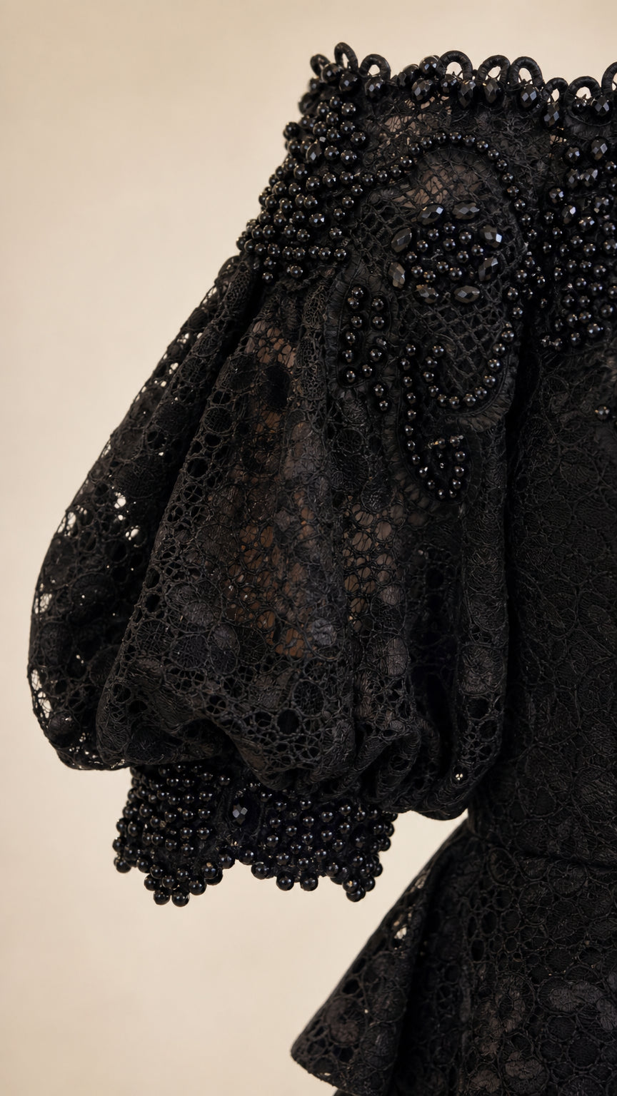 Close-up detail of black floral lace fabric with intricate beadwork along the sleeve cuff and neckline
