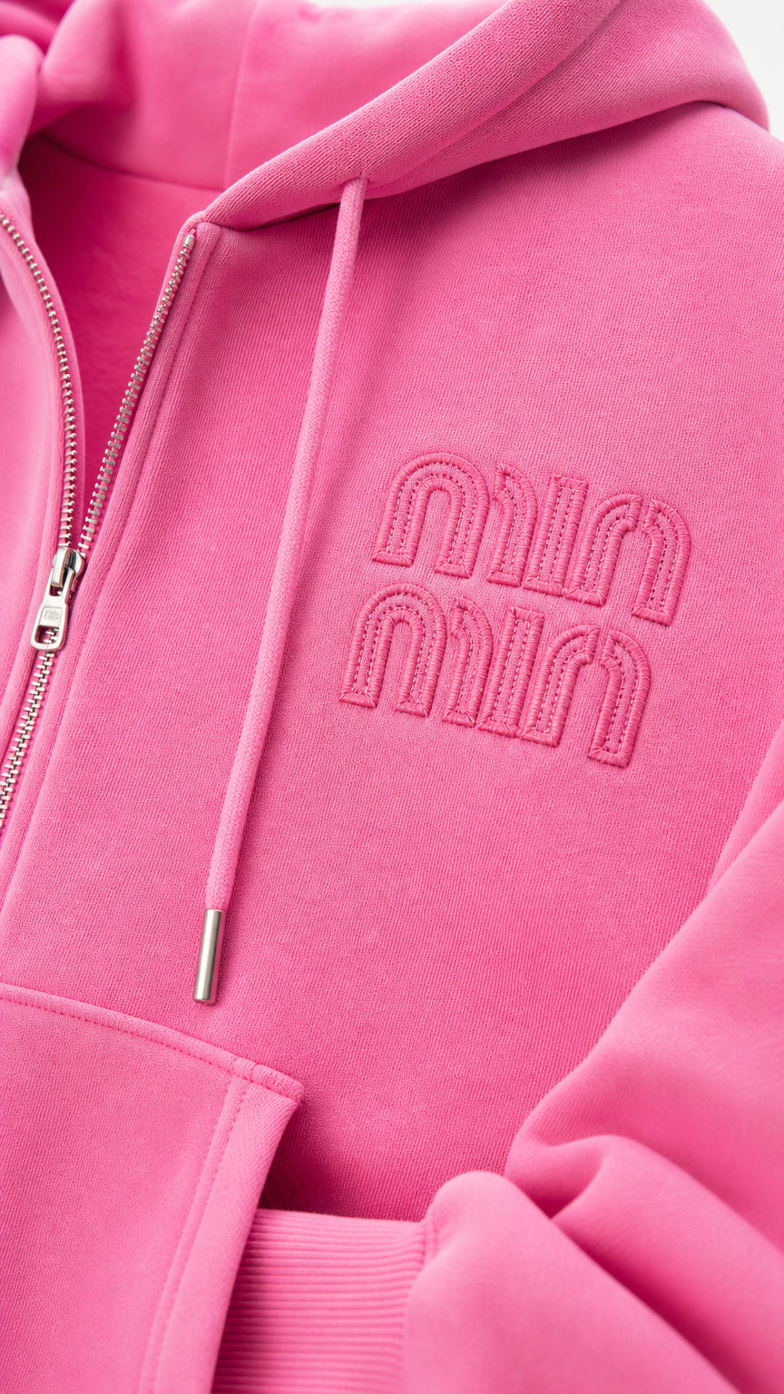 Close-up detail of pink zip hoodie featuring tonal embroidered chest logo and metal zipper