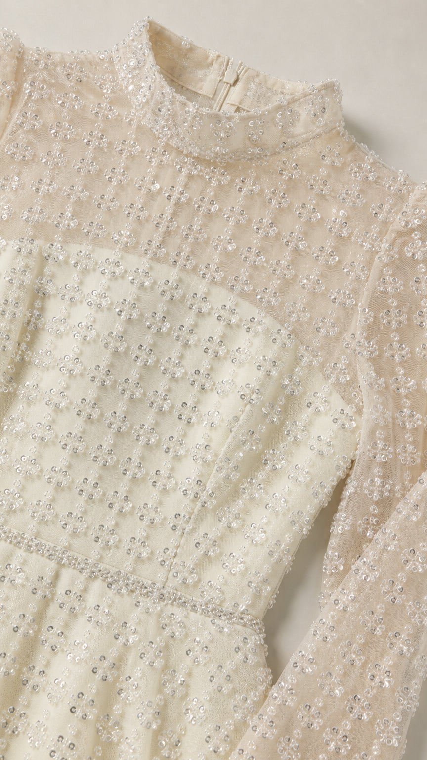 Close-up detail of sheer mock neckline and shimmering grid embellishments on ivory dress