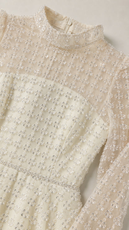 Close-up detail of sheer mock neckline and shimmering grid embellishments on ivory dress