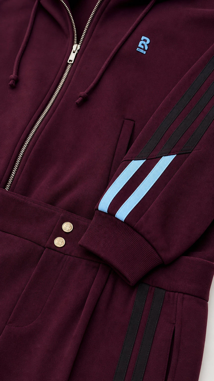 Close-up detail of burgundy zip-up jacket cuff, sleeve stripes, and waistband buttons