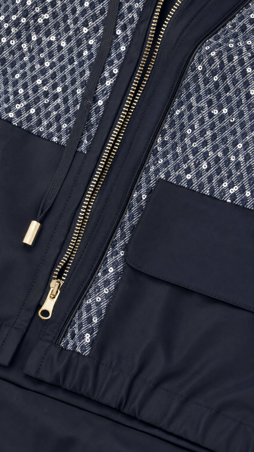 Close-up detail shot of the black jacket featuring sparkling sequin panels, metallic zipper, and drawstrings