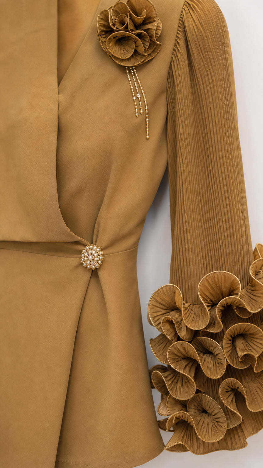 Close-up detail of 3D fabric flower corsage, jeweled button, and pleated ruffle sleeve in camel