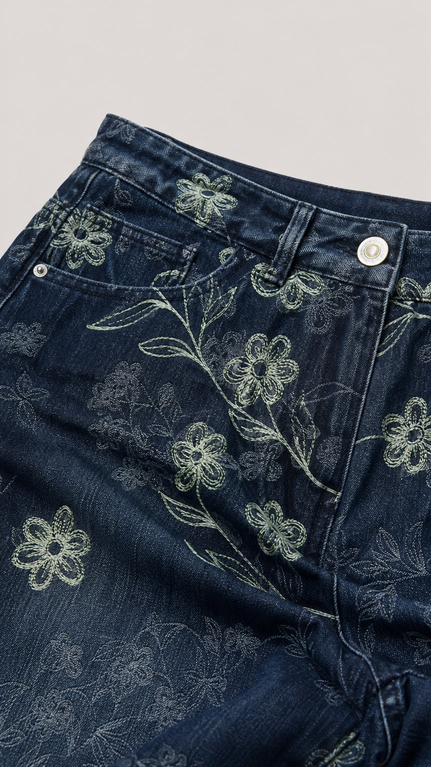Close-up detail of Denim Blue pants showing intricate floral embroidery, pocket, and button