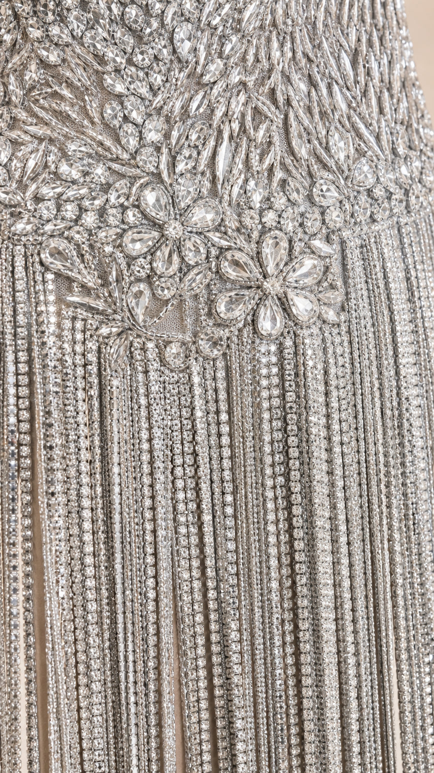Close-up detail of crystal embellishments and beaded fringe on silver dress bodice