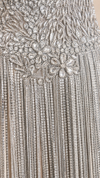 Close-up detail of crystal embellishments and beaded fringe on silver dress bodice